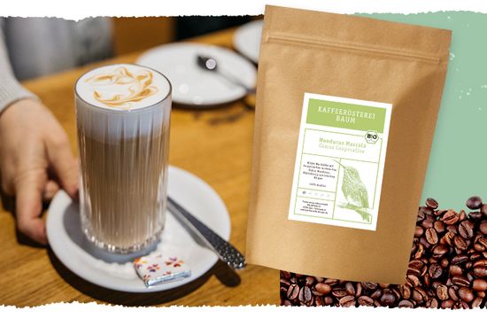 KI generiert: Das Bild zeigt ein Glas mit einer verzierten Kaffeespezialität auf einem Teller neben einer Packung Kaffee von der "Kaffeerösterei Baum". Im Hintergrund sind Kaffeebohnen zu sehen.