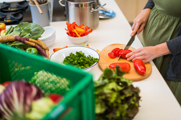 Eine schwangere Frau schneidet Tomaten in einer Küche, umgeben von frischem Gemüse.