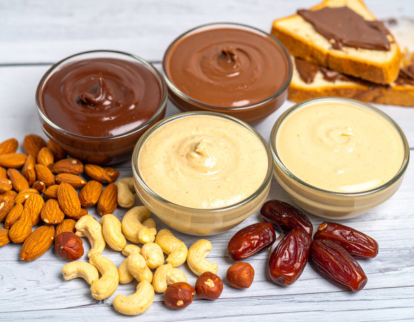KI generiert: Schüsseln mit Nusscremes und Nüssen auf einem Tisch, dazu Datteln und Nuss-Nougat-Brot.