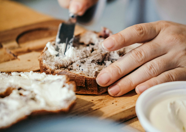 KI generiert: Eine Hand bestreicht Brot mit Frischkäse auf einem Brett.