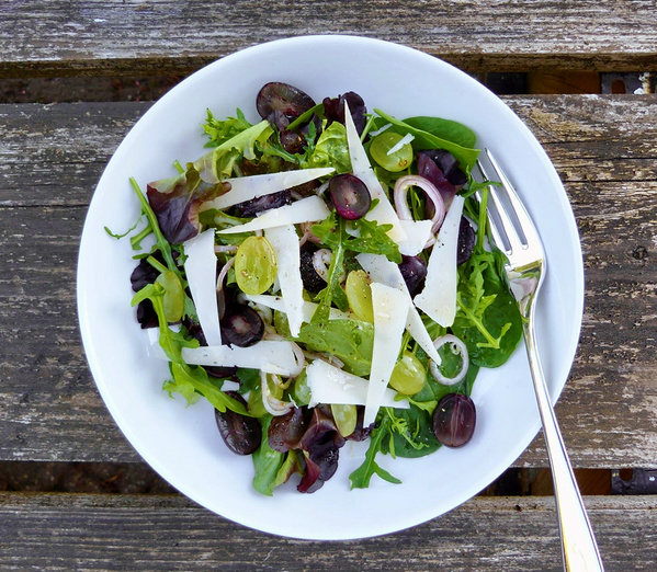 KI generiert: Ein frischer Salat mit Trauben, Zwiebeln und Käse auf einem Holztisch.