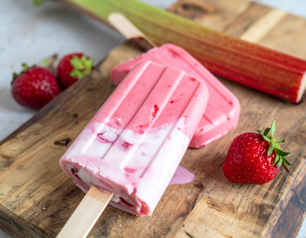 KI generiert: Erdbeer-Rhabarber-Eis am Stiel auf einem Holzbrett mit frischen Erdbeeren und Rhabarber.