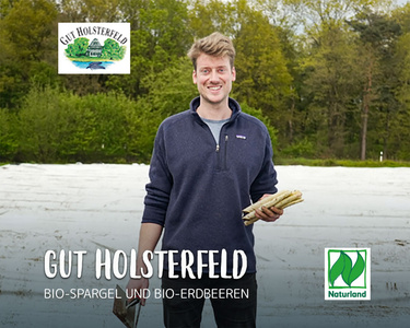 Ein Mann hält Spargel auf einem Feld. Text: "Gut Holsterfeld, Bio-Spargel und Bio-Erdbeeren".