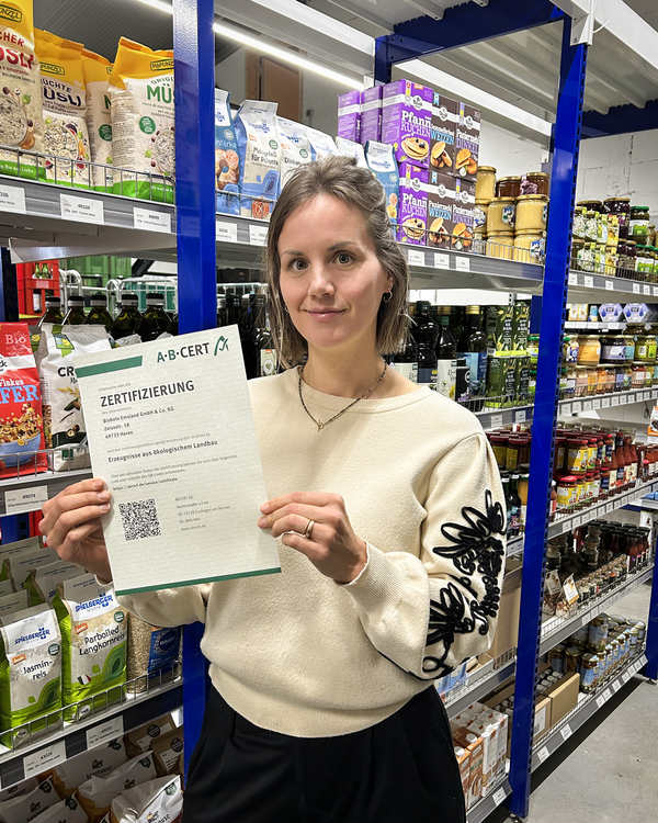 KI generiert: Eine Frau hält ein Zertifikat in einem Bioladen. Text: "Zertifizierung... Erzeugnisse aus ökologischem Landbau".