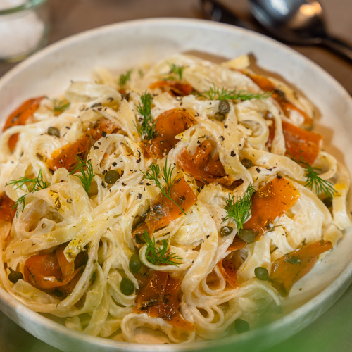 KI generiert: Ein Teller mit cremiger Pasta, garniert mit Dill, Kapern und Tomatenstücken.