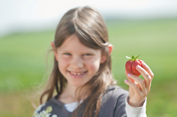 KI generiert: Ein Kind hält eine frische Erdbeere und lächelt im Freien.