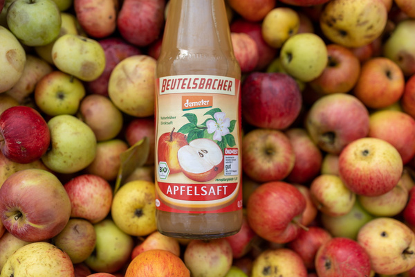 Flasche Beutelsbacher Apfelsaft auf einem Bett aus Äpfeln. Text: "Beutelsbacher Apfelsaft".