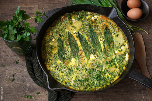 KI generiert: Eine Kräuterfrittata in einer Pfanne, umgeben von frischen Kräutern und Eiern.
