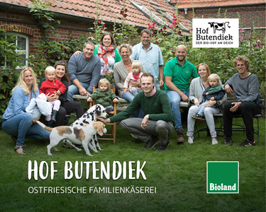 Eine Familie sitzt im Garten. Text: "Hof Butendiek OSTFRIESISCHE FAMILIENKÄSEREI".