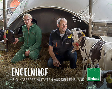 Zwei Menschen im Stall mit Kühen, daneben das Logo von "Engelnhof" und "Bioland". Text: "BIO-KÄSESPEZIALITÄTEN AUS DEM EMSLAND".