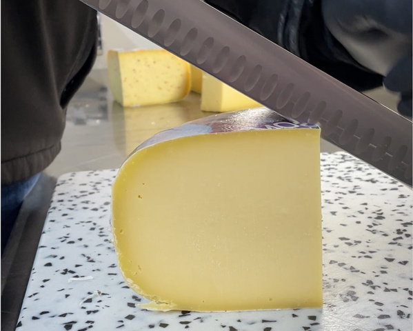 KI generiert: Ein Käsestück wird mit einem Messer auf einem Schneidebrett geschnitten.
