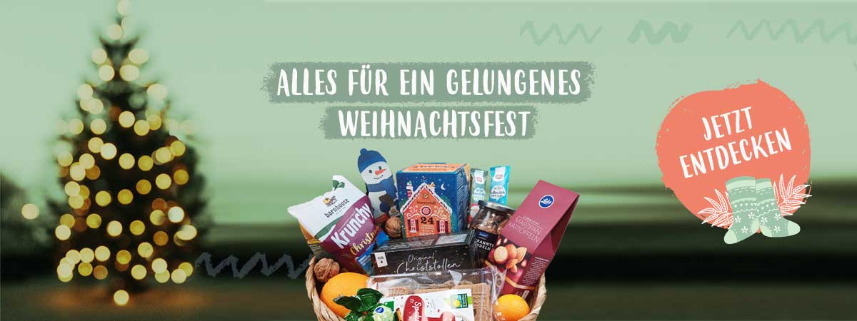 KI generiert: Geschenkkorb vor unscharfem Weihnachtsbaum. Text: "Alles für ein gelungenes Weihnachtsfest. Jetzt entdecken".