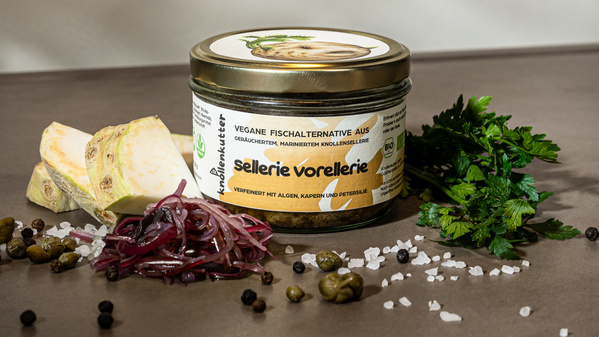 KI generiert: Ein Glas mit veganer Fischalternative "Sellerie Vorellerie", umgeben von Sellerie, Zwiebeln, Petersilie und Kapern.