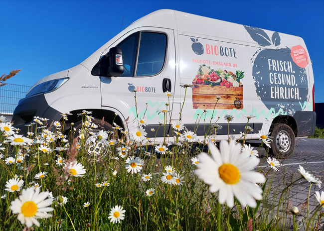Ein Lieferwagen mit "BIO BOTE" steht hinter einer Wiese voller Gänseblümchen. Text: "FRISCH. GESUND. EHRLICH."