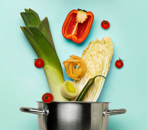 KI generiert: Ein Topf mit Lauch, Paprika, Tomaten, Pasta und Chinakohl auf blauem Hintergrund.