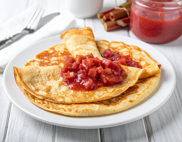 KI generiert: Pfannkuchen mit roter Fruchtsoße auf einem weißen Teller, im Hintergrund ein Glas mit Soße.