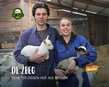 wei Personen halten Zicklein in einer Scheune.   Text: "DE ZEEG DEMETER ZIEGEN-HOF AUS WEENER"