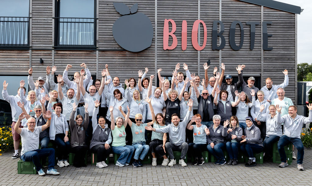 KI generiert: Eine Gruppe von Menschen posiert vor einem Gebäude mit dem Schriftzug "BIOBOTE".