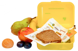 KI generiert: Gelbe Brotdose mit Brot, Obst und Gebäck. Text auf Papier: "FRUCHT Bombe" und Markenlogos.