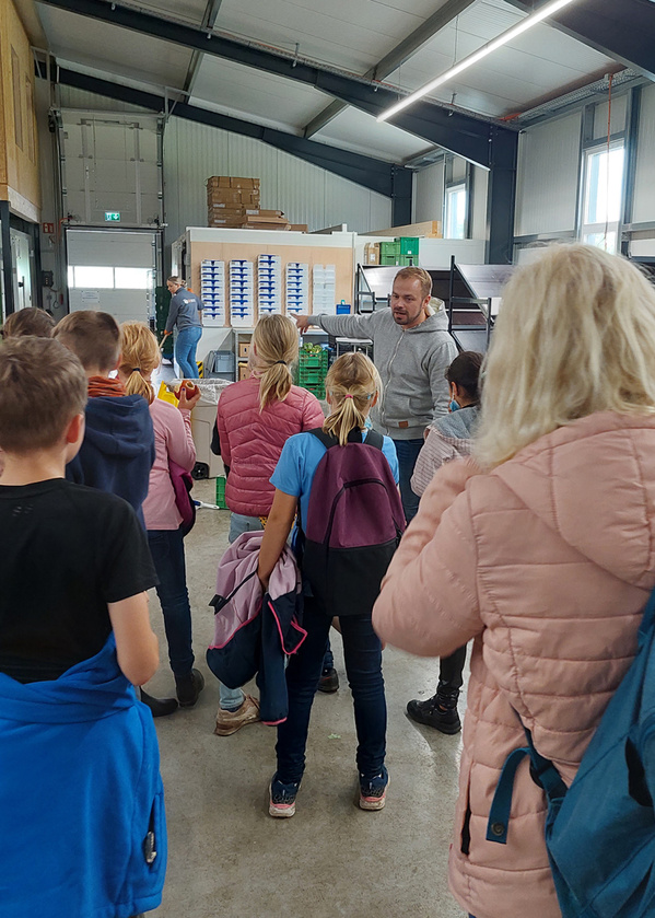 KI generiert: Person erklärt einer Gruppe in einem Lagerraum etwas. Keine Textinhalte erkennbar.