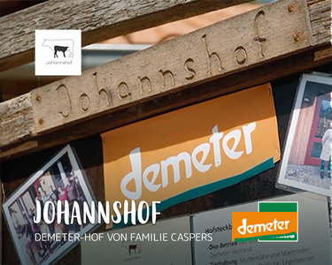 Schild des Johannshofs mit Demeter-Logo und Fotos. Text: "JOHANNSHOF DEMETER-HOF VON FAMILIE CASPERS".