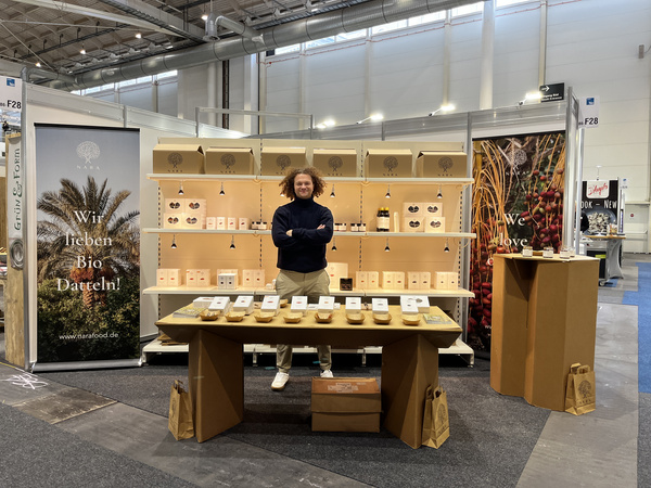 KI generiert: Eine Frau steht an einem Stand mit Bio-Datteln. Text: "Lieben Bio Datteln!"
