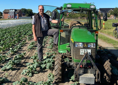 Bauer Dietmarvom Bioland Gemüsehof Weßling steht neben einem grünen Traktor auf einem Feld voller Pflanzen.