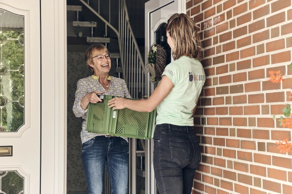 Lisa übergibt Biokiste an Kundin bei ihrer Haustür