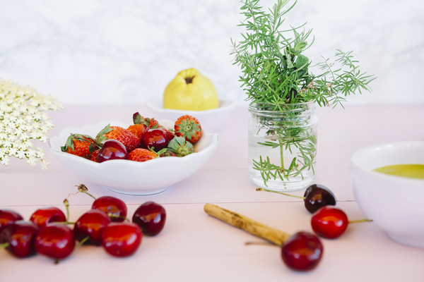 KI generiert: Frische Erdbeeren und Kirschen in einer Schale, Kräuter in Glas und Tee auf Tisch.