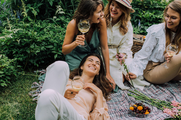KI generiert: Vier Frauen lachen und trinken Wein bei einem Picknick im Grünen.