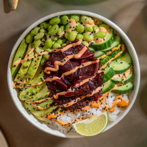 KI generiert: Eine bunte Poké Bowl mit Avocado, Edamame, Gurken und Limette, dekoriert mit Sauce und Sesam.